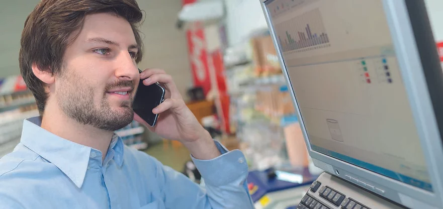 Mann mit kurzen dunkeln Haaren sitzt vor einem Computer und telefoniert.